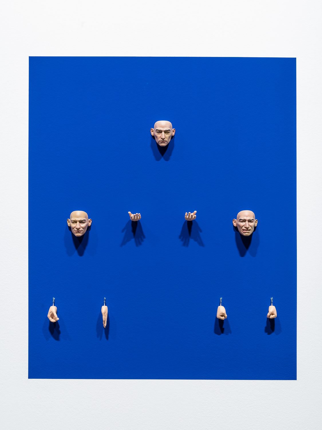 Cécile B. EvansA man in progress, 2017Hand-carved clay and wood hands, 3D sculpted and printed, hand painted resin masks, hooks, chroma blue screen paint120 x 100 x 10 cm